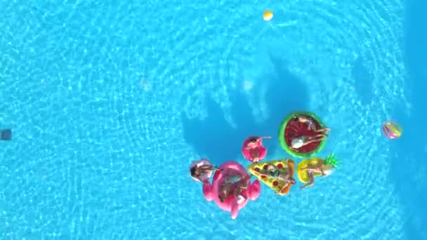 Luftkopierraum verspielte Mädchen und Jungs, die auf fallenden Schwimmern im Pool liegen. glücklich lächelnde Freunde genießen den Sommerurlaub auf aufblasbaren Ananas, Pizza, Flamingo, Wassermelone und Donut schwimmt