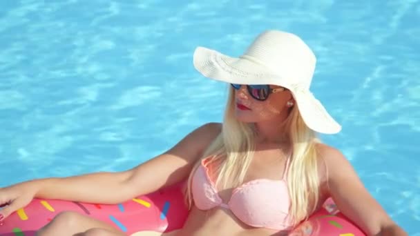 Zpomalené Detailní záběr: Krásná blond dívka relaxační na plovoucí nafukovací růžový prstencový. Mladá žena Kráska v bikinách se těší letní prázdniny na růžové floatie v bazénu na horký slunečný den