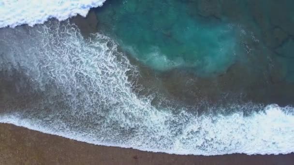 透き通った海が美しいバリ島のエキゾチックなビーチでサンゴ礁の破壊で空中トップ ダウン スローモーション泡波 ターコイズ ブルーの海の海岸の浅瀬で岩浅瀬にはねかける — ストック動画