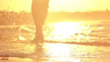 Ağır çekim yakın Lens Flare Up: kum plajındaki su sıçramasına altın günbatımında çalışan aktif genç adam. Güzel sarı sabah güneş doğarken sığ okyanus su koşu tanınmaz Erkek atlet