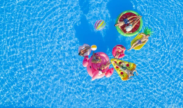 空中トップダウンコピースペース プール内のカラフルな浮遊物に横たわっている女の子と筋肉の男をフィットさせ ボールでバレーボールをプレイします インフレータブルラウンジャーで水に浮かぶ楽しい夏休みの友人 — ストック写真