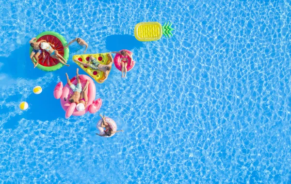 空中トップダウンコピースペースプールでカラフルな浮遊物に横たわっている女の子と筋肉の男にフィットし 太陽の下でリラックスしてぶら下がっています インフレータブル枕の上に水に浮かぶ楽しい夏休みの友人 — ストック写真