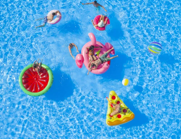 陽気な友人は 夏のプールパーティーでカラフルな浮遊物を楽しんでいます 遊び心のある男と女の子潮吹き水と取りますSelfiesオンインフレータブルピザ ドーナツ フラミンゴとスイカフロート — ストック写真