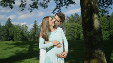 Kucaklanan hamile çift güneşli bir günde bir ağacın altında durarak samimi bir an paylaşıyor. Heyecanlı genç anne-babalar hamilelik harikaları zevk olmak. Karı koca bebeğin doğmasını bekleyemez.
