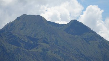 Yakın: Devasa aktif yanardağ doğru bulutlu gökyüzü kule Endonezya. Nefes kesici dağ uzaktan ateş ağaçları ile dağınık. Behemoth dağın Mount Bulutların arasından yükselen Batur.
