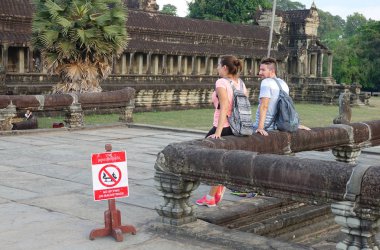 Angkor Wat, Kamboçya, Nisan 2017: İki saygısız Kafkas turistler çok dokunaklı ve antik Angkor Wat çürüyen kalıntıları üzerinde oturan insanlar yasaklayan işaret yanında korkuluk taş oturmak