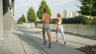 Sportif genç çift varlıklı mahallede hoş sakin avenue aşağı çalışır. Genç adam ve kadın atletik fiziksel ile birlikte güneşli bir öğleden sonra şehirde iş dışarı. Sportif açık hava etkinliği