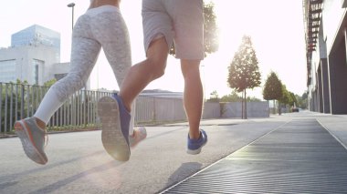 Düşük Açı, Lens Flare: Güneşli bir bahar sabahı asfalt şehir sokaklarında koşarak Uygun Kafkas çift bağ. Güzel bir bahar sabahı şehirde açık havada egzersiz iki uygun arkadaşlar.
