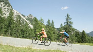 Yol bisikletçi dalgalar ve kolayca yenilikçi elektrikli bisiklet gurl tarafından overtaken Yorumlar mücadele. Sundress pedallar pro dağ bisikleti rider güneşli yaz aylarında geçmiş kadında sarışın şehir.