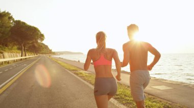 Yakından bakınca, güneş patlaması: Tanınmayan genç aktif çift güzel güneşli okyanus avenue çalışır. Sportif beyaz kız ve erkek arkadaşı yaz tatil koşu üzerinde mükemmel altın yaktı Sahil yakınındaki