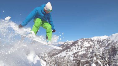Yakın: Profesyonel snowboard mükemmel bir karlı tepeden aşağı sürmek ve havadaki yüksek atlar. Snowboard üzerinde aşırı sürücüsü bir karla kaplı kenardan bir güzel kış gününde görkemli Dağları atlar.