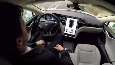 Graz, Avusturya - 2 Şubat 2017: genç işadamı lüks Tesla Model S araç otomatik etkin otomatik pilot kendi kendine sürüş sistemi ile iş için seyahat. Elektrikli araç yolda kendisi tarafından sürüş