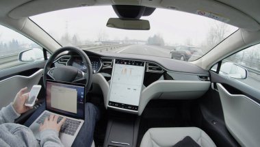 Tesla özerk araba-Şubat 4, 2017: direksiyon tutun ve karayolu üzerinde kontrol altına almak için sürücü dikkat talep Self-driving Tesla Model S araba otomatik pilot. Laptop ve cep manifatura üzerinde çalışan adam