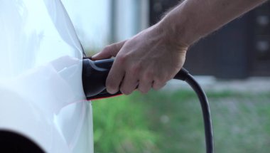 Yakın: elektrikli araç şarj istasyonu supercharge hızda taktıktan tanınmayan adam. Lüks beyaz elektrik Tesla araba şarj. Çevreye duyarlı erkek onun elektrikli araç şarj