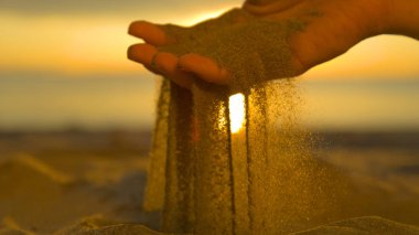 CLOSE UP: Unrecognizable woman grabs a handful of dry sand and lets it fall between her fingers. Young female traveler on a sunny beach in Fiji sifts coarse beach sand between her gentle fingertips.