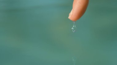 MACRO, DOF: Cool shot of holiday resort being reflected in tiny water droplet slipping off of unrecognizable woman's fingertip. Glistening drop of pool water barely holding on to young girl's finger. clipart
