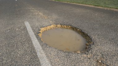 Yakın: Yolun ortasında büyük çukur bulanık su ile doldurulur. Büyük su dolu delik uzak kırsal yol ortasına gelecek trafik için büyük bir tehlike sunar. Yıpranmış karayolu ağı.