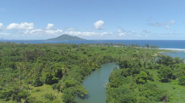 AERIAL: Flying along tropical river estuary and towards distant mountainous islet on sunny summer day on remote island. Stunning exotic vegetation overgrowing spectacular untouched beaches of Vanuatu.