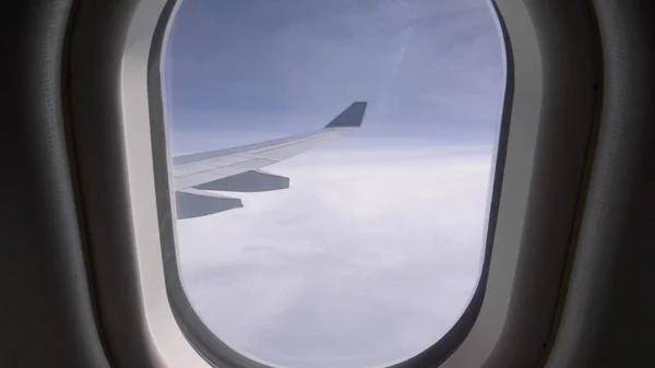 Pov 現代の飛行機の無限の雲と大きな金属の翼で小さな窓を通して見て 大西洋横断ジェット機の窓側座席からの広大な空間と厚い雲の素晴らしい眺め — ストック写真
