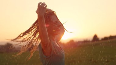 Kadar yakın, Lens Flare: Çekici sarışın saçlı kadın şakacı yatıştırıcı yaz yağmur altında döner. Genç kafkas kadın dansçı dansları kırsal güzel bahar akşamında yağmurda.