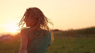 Kadar yakın, Lens Flare: açık havada günbatımında taze bahar yağmurda dans kaygısız sarışın bir kadın. Güzel kız spin nefes kesen bir portakal güzel kırsalında şakacı yaz akşam yaktı.