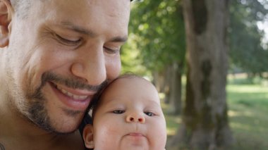 Yakın plan, Kopya Uzay: Büyük dövmeli baba yeşil parktaki küçük kızıyla paha biçilmez güzel anları paylaşıyor. Sevgi dolu genç baba kıymetli yeni doğmuş kızını kucağında tutuyor ve baharın tadını çıkarıyor..