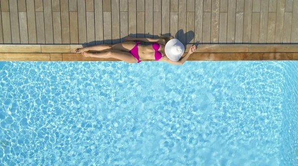 トップダウン コピー領域 魅力的なフィット体で認識できない女性は 透き通ったプールで日光浴をしながら彼女の顔にスタイリッシュな白い帽子を置きます リラックスした若い女性観光客の太陽の日焼け — ストック写真