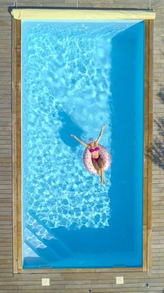 トップダウン 夏に低温ドーナツ フローティング ツールバーのピンクの水着でのうれしそうなフィットの女の子 空気注入式ドーナツの透き通ったプールの周り浮かんでいる間豪華な白人女性日焼け — ストック写真