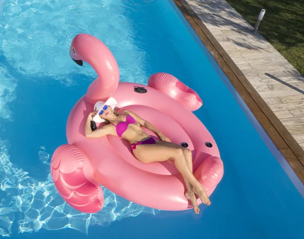 快乐的年轻女子躺在一个大的充气火烈鸟漂浮在令人敬畏的私人游泳池闪闪发光的烈日夏天 金发白种人女孩有乐趣日光浴在凉爽的浮选 — 图库照片