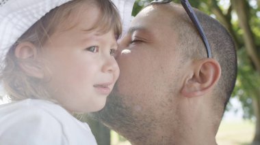 Sevgi dolu baba neşeleniyor ve kucağında oturan masum kızına fısıldıyor. Mutlu baba, huzur dolu yeşil parkta yürürken küçük tatlı kızıyla konuşuyor..
