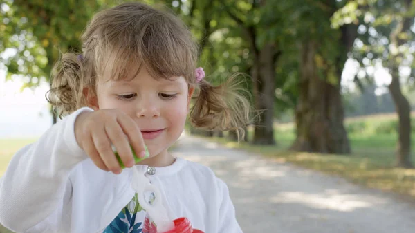 风趣的小女儿在全家去公园旅游的过程中吹泡泡肥皂泡 可爱的高加索小女孩 留着可爱的辫子 在阳光灿烂的林荫大道上嬉戏 吹着泡沫 — 图库照片