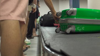 CLOSE UP: Travelers from all over the world pick up their luggage off spinning rubber carousel. Unrecognizable people waiting and collecting their suitcases after a long flight to Don Mueang airport.
