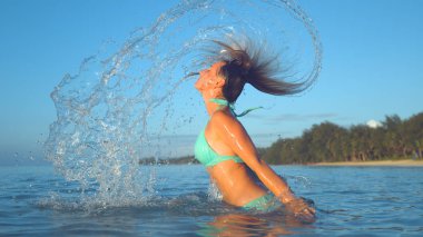 Yakın: Akşam güneşi ıslak saçlarını geriye doğru okyanustan saygısız ve parlak su damlacıkları havada püskürtme genç kadın parlar. Beyaz kız onu tatil tropikal beach yakınındaki zevk.