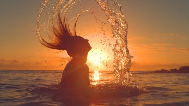 Siluet, Close Up, Lens Flare: Nefes kesen turuncu sabah güneş ışınları uzun saçları ile deniz suyu sıçramasına bilinmeyen kadın kendini. Tanınmayan kız okyanusta güneş doğarken oynamak tatil.