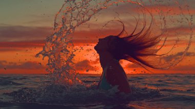 Kadar yakın, siluet: Yaz tatili oynak kadın saçlarını okyanustan çırpar ve su gökyüzünde güneş doğarken sıçramalarına. Genç kadın turist ferahlatıcı okyanusta onu tatil keyfi.
