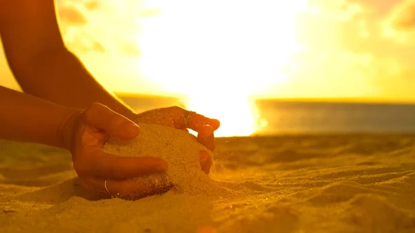 クローズ アップ 認識できない女性観光客を散乱させる砂のコース彼女の優しい指先を美しい夕暮れ時 ビーチで砂で遊ぶ女の子に輝く夏の日の出の映画のようなショット — ストック写真