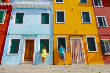 Düşük açılı: Genç erkek ve kadın turist renkli evler güneşli Burano, İtalya tarafından konuşmak durdurmak. Güzel çift pozlar Venedik kanalları seyir pitoresk binaları önünde.