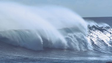 CLOSE UP: Sparkling drops of water fly in the air and create a beautiful mist around the blue breaking tube wave crashing into the rocks on the spectacular sunny coast of breathtaking Easter Island.