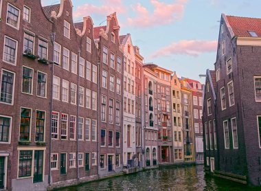 Güzel Amsterdam'ın tarihi binaları geçmiş günbatımında çalışan küçük kanal. Güzel atış, dar kanal ve Hollanda'da nefes kesen Avrupa mimari sakin yaz akşamı.