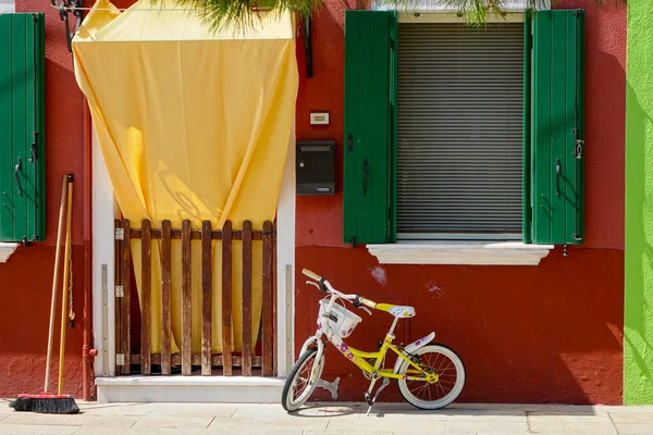小玩具自行车和扫帚在世界著名运河附近的一个深橙色威尼斯人的房子前休息 在意大利布拉诺空荡荡的五颜六色的街道上废弃的自行车的风景如画的镜头 — 图库照片