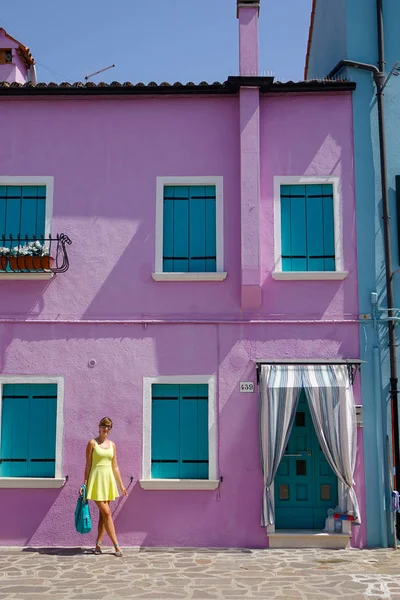 愉快的高加索妇女在观光旅行站在一个美丽的紫色房子前 在一个阳光明媚的意大利岛屿 年轻的女性旅行者在威尼斯五颜六色的空旷街道上摆姿势时微笑着 — 图库照片