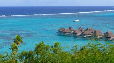 Small emerald ocean waves splash and approach the wooden bungalows of cool luxury holiday resort in French Polynesia. Picturesque view of the exotic island and awesome overwater villas in Thailand.