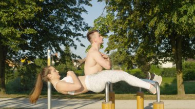 Atletik genç adam ve kadın oturup ups güneşli parkta paralel bar. Neşeli egzersiz ortakları eğleniyor doğada egzersiz. Gömleksiz sevgiliyi yaz eğitim tarafından zevk