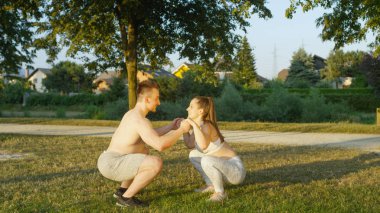 Güneşli parkta vücut ağırlığı ağız kavgası yaparken elele gülümseyen iki. Neşeli sevgiliyi ağız kavgası birlikte doğada yapıyor. Atletik kadın ve gömleksiz adam birlikte eğitim.