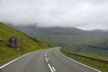 Dik bir yokuş güzel Faroe Adası doğada etrafında sarma doğal asfalt yol. Canlı yeşil doğa ile soğuk ve sisli sabahı çalıştıran boş ülke Trail muhteşem atış.