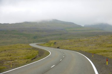 Boş asfalt yol rüzgarlar Faroe Adaları çimenli vahşi doğada sisli sabahı dağ pitoresk. Beyaz bulutlar kırsal boş sokakta azalan muhteşem çekim.