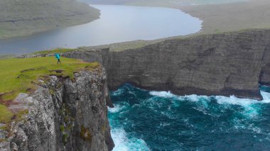 Anteni: uçurumun kenarında siyah kayalıklarla ve mesafe sakin gölde isabet okyanus doğal manzaralı doğru hiking tanınmaz halde genç bir kadın. Faroe Adaları'nın nefes kesen kıyılarında.
