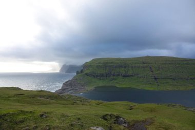 Pitoresk çok yüksek kayalıklarla ve Faroe Adaları okyanusta büyük karanlık fırtına bulutları toplanıyor. Engebeli İskandinav Shore tarafından beyaz bulutlar kaplı sarp çimenli tepeler ile nefes kesen manzarası.