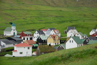 Faroe Adaları'nda dik çimenli dağlar altında canlı yeşil kırsal sakin kasaba. Ismarlayarak pastoral kırsal ortamda sakin bir köy. Güzel küçük şehirde yemyeşil çayırlar.