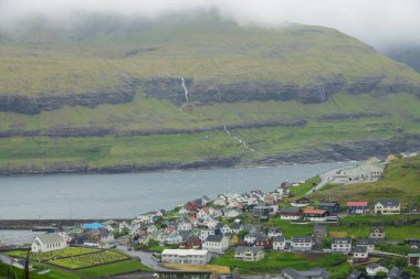 Hava: waterfront village güzel dağ Stream mükemmel manzaralı doğru uçan. Atış sessiz kıyı kenti yeşil Faroe Adaları'nın kayalık tepeden aşağı akan nehri çarpıcı.